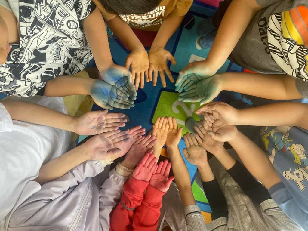 Children at OWIS Osaka taking part in a group activity promoting positive shared values. The kids have their hands together in a circle and are painted different colours