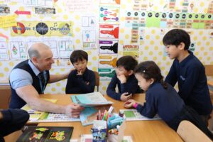 Teacher Helping students to read a book in a classroom at One World International School